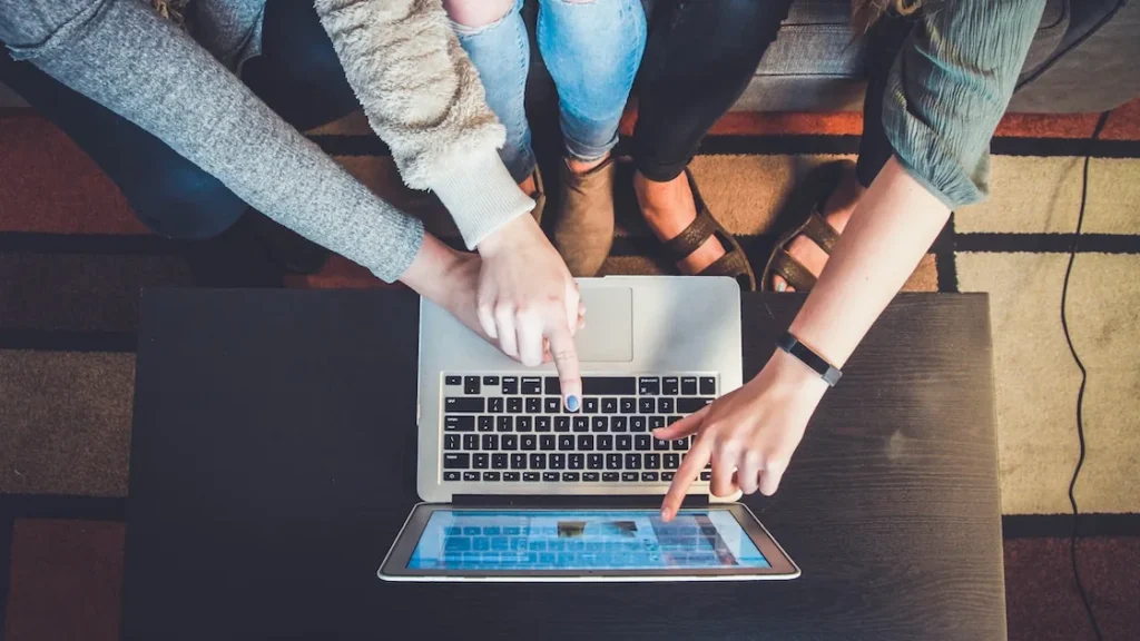 Three people gathered around a laptop, pointing at the screen as they browse online together.