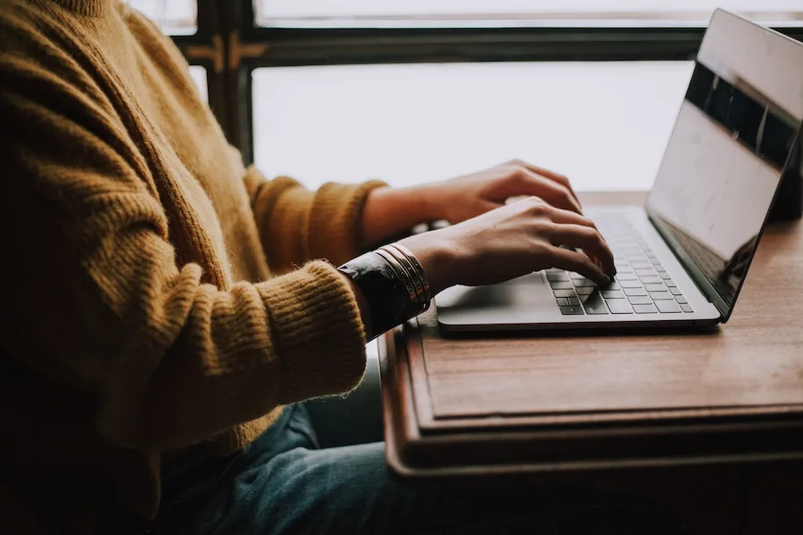 A salon owner sitting at a table, typing on a laptop while reviewing their business admin.