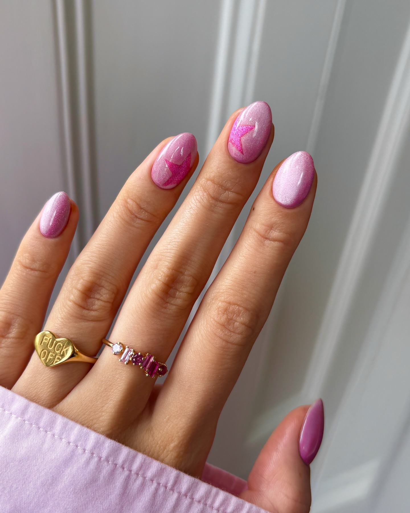 Pink cat eye nails with a glossy finish, featuring pastel shades and delicate gradients, worn with gold rings. Credits @thenaillologist