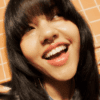 Smiling person with long dark hair, fringe, and nose ring against an orange tiled background.