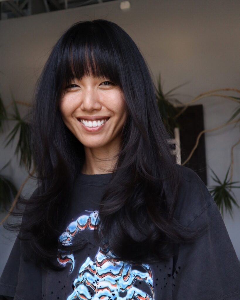 A woman with long, thick dark hair and a blunt fringe cut straight across the forehead for a sharp, dramatic effect.