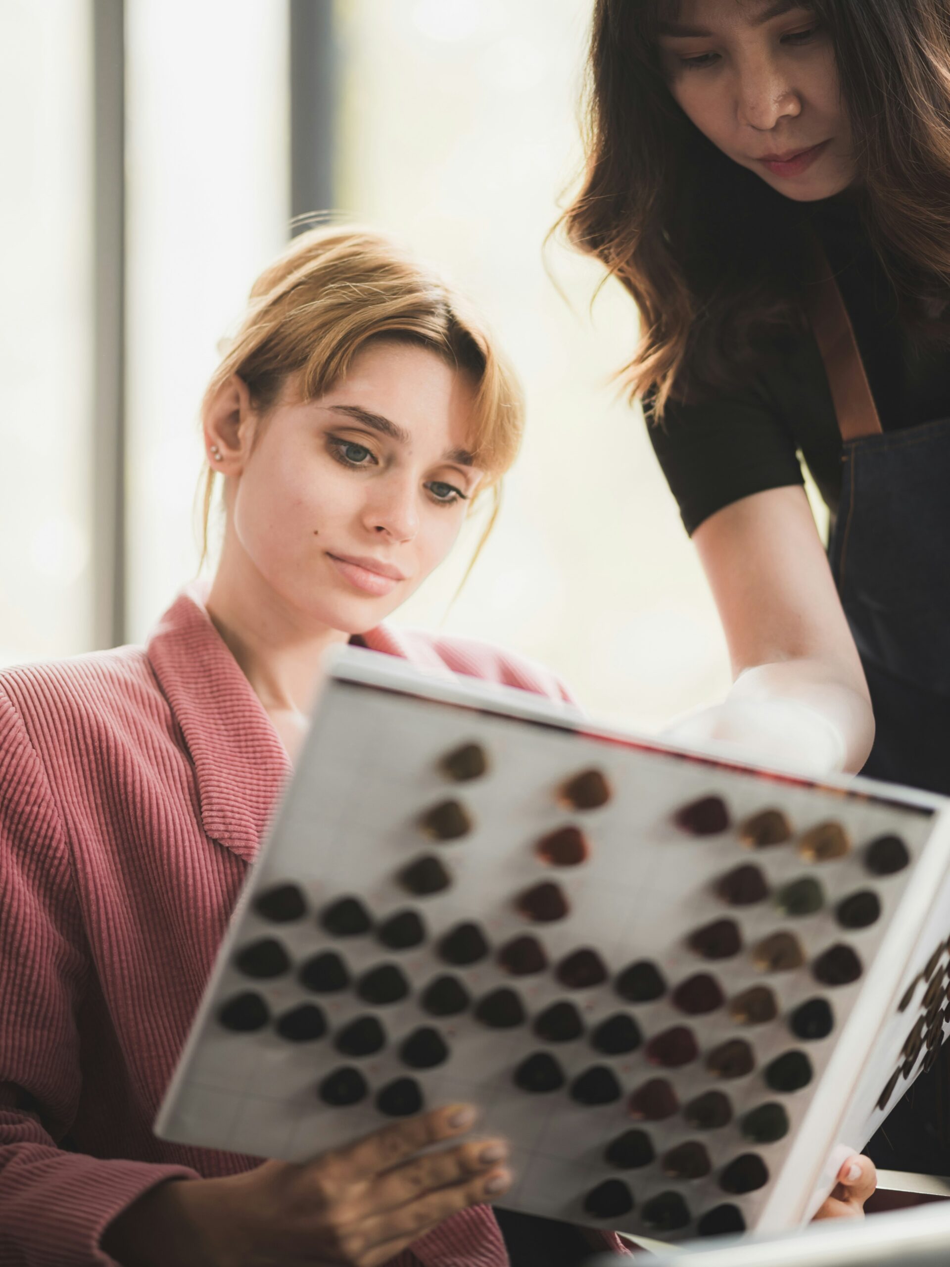 Client sits in a hairdressers looking at a book of colour swatches with a stylist