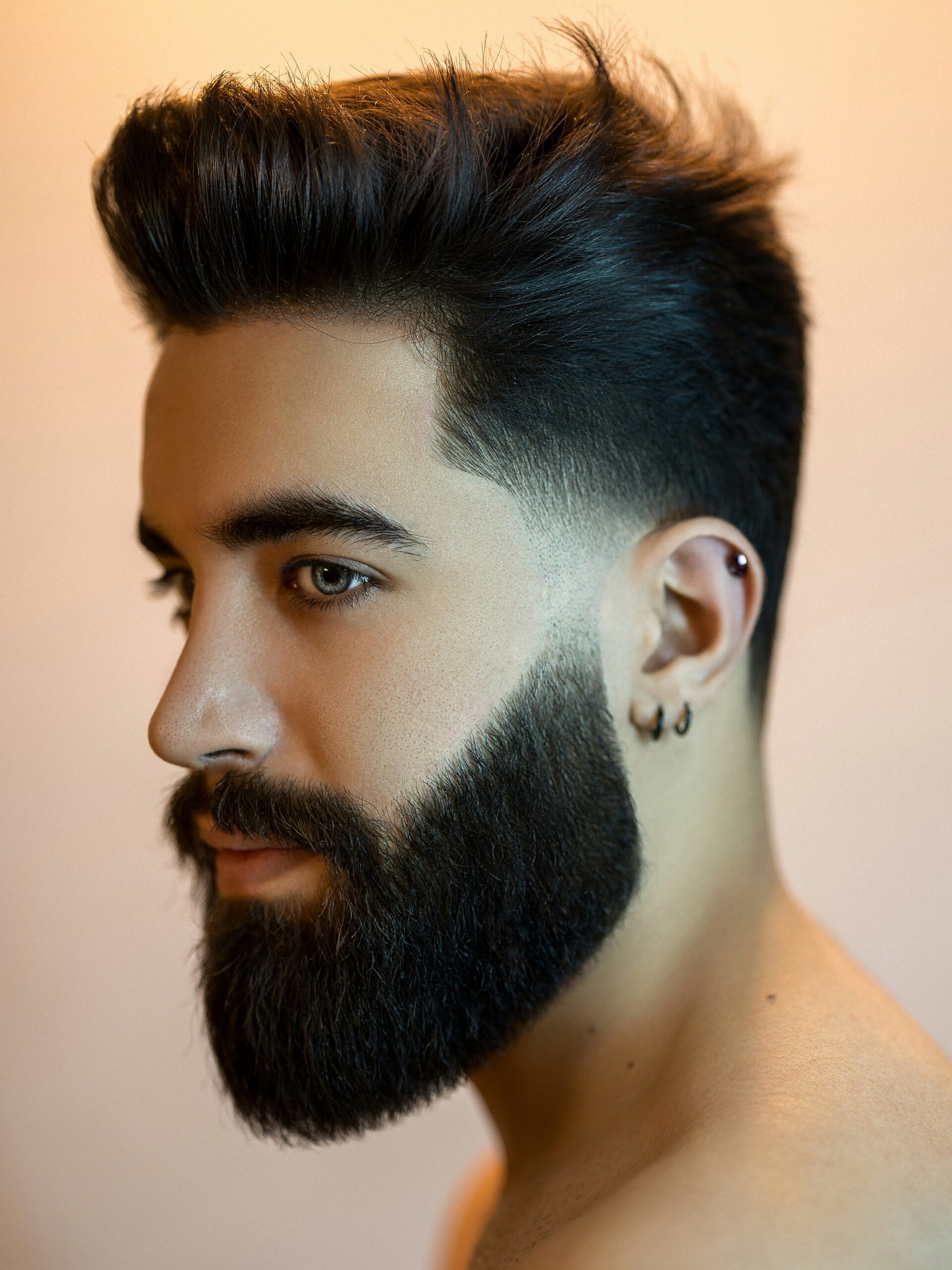 Man with an oval face shape and dark hair wearing a low taper fade with volume and a beard