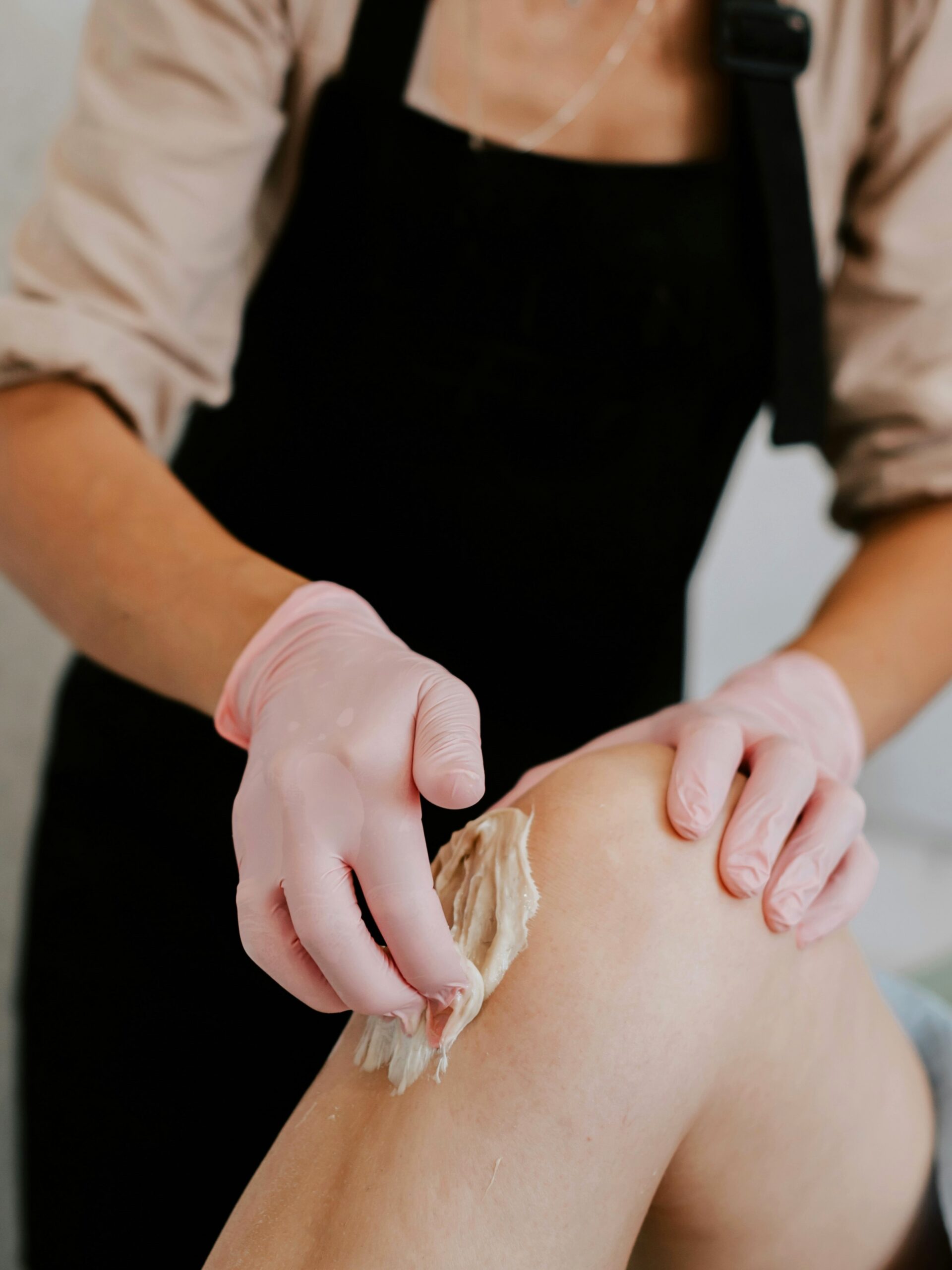 Side view of practitioner applying wax to a client’s leg as she lies comfortably on a treatment bed in salon