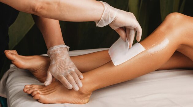 Close-up of practitioner waxing a client's lower leg in a bright, clean salon
