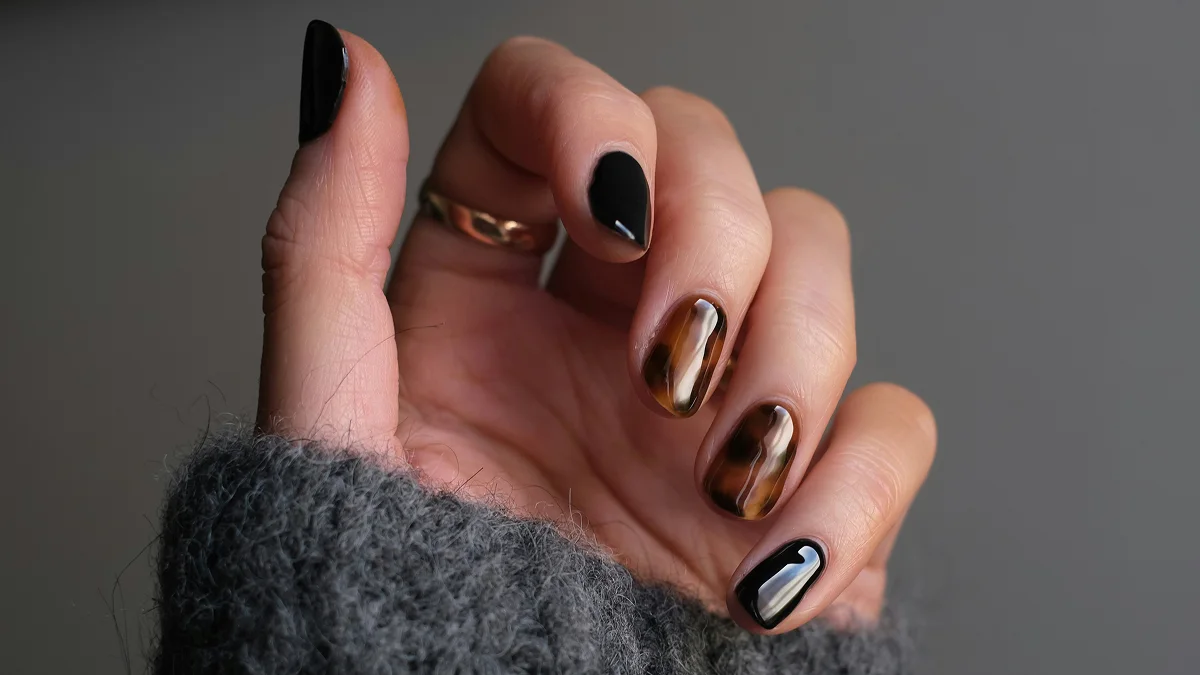 Close-up of a hand with short nails and a shiny gel manicure in black and animal print shades