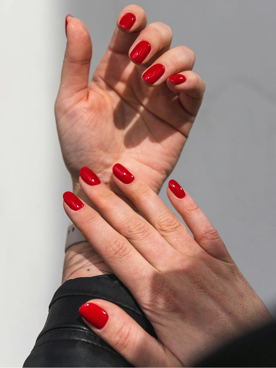 Close-up of a woman’s forearms wearing a black leather jacket and showing a glossy red gel manicure