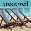 Two striped wooden deckchairs on the sand in front of pastel-blue beach huts on the Versilia coast