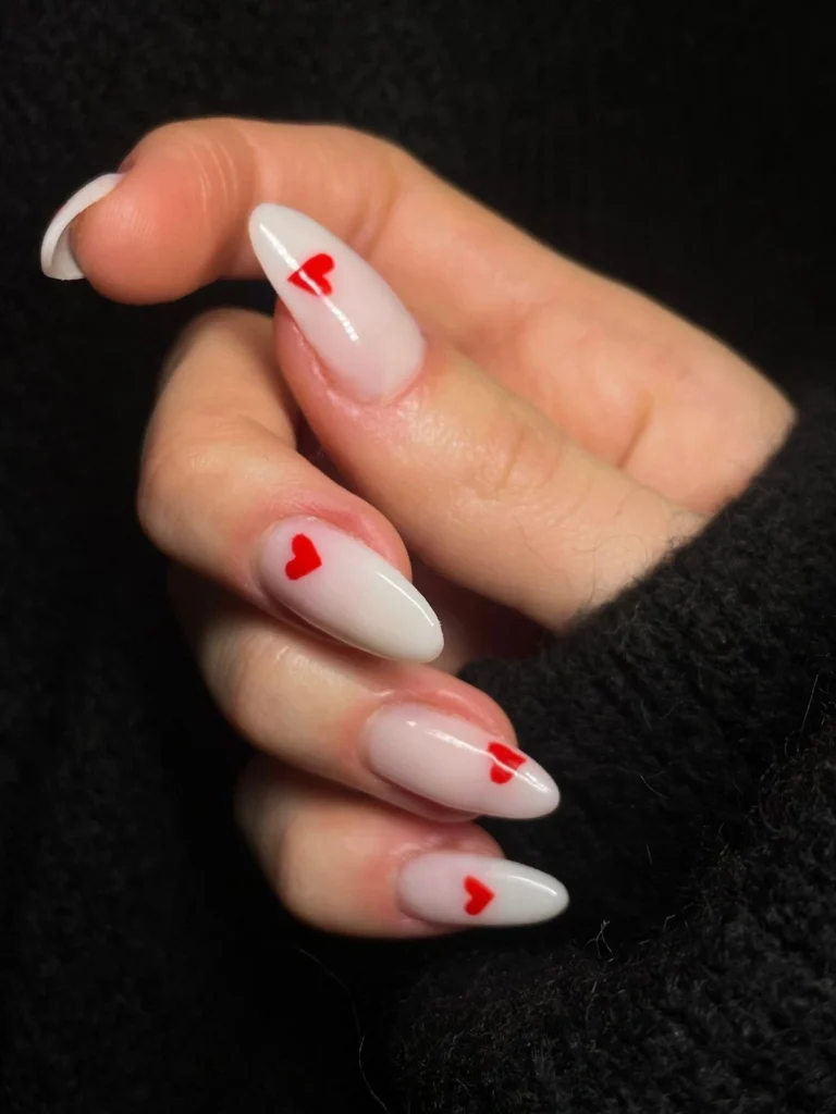 Close-up of a woman's hand with white almond-shaped acrylic nails decorated with small red hearts