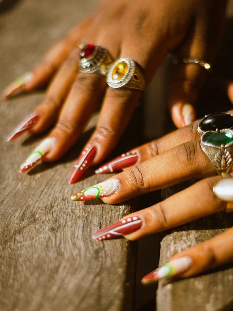 Close-up of a woman's hands with stiletto-shaped acrylic nails in red and white decorated with green and yellow dots and swirls