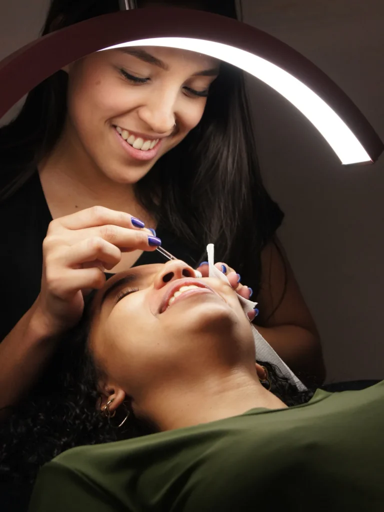 Close-up of a technician applying eyebrow tint to a client who is relaxing on a treatment bed in salon