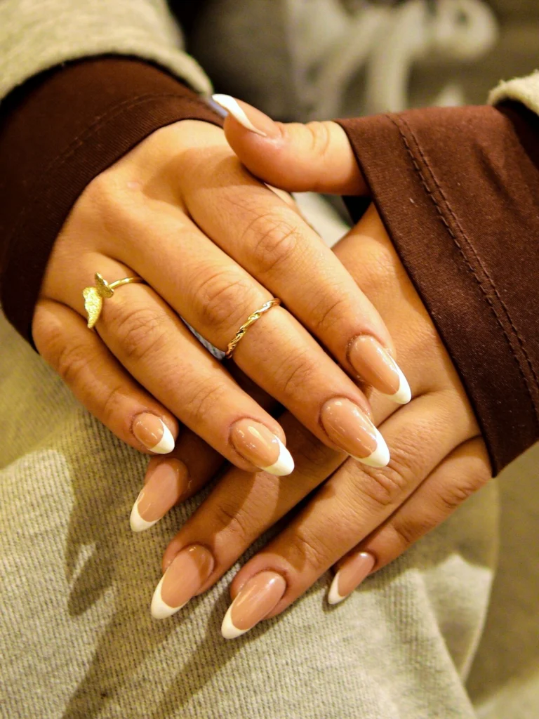 A woman’s hands show a bold French tips manicure with a beige and white combination on long almond nails