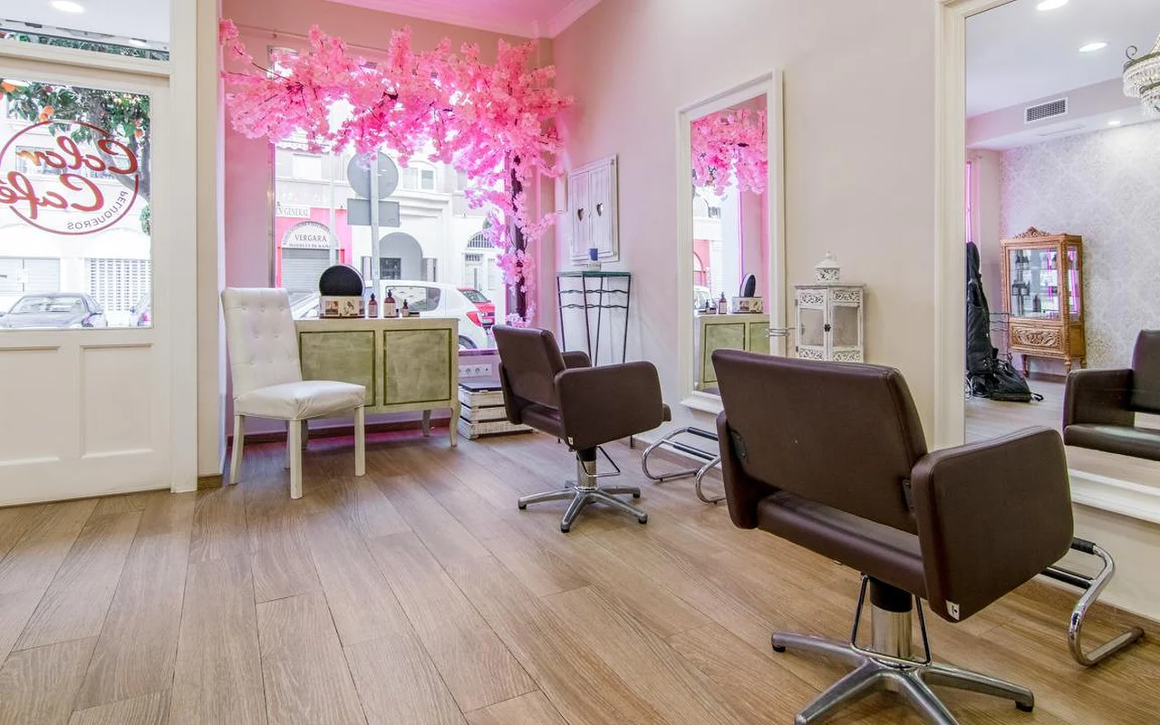Inside Color Café Peluqueros in Torremolinos, a pink-walled hair salon with brown styling chairs, large mirrors and a pink cherry-blossom display in the window.