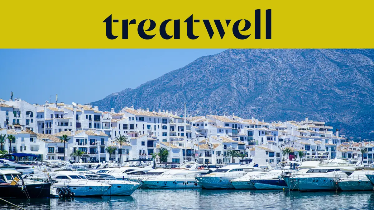 Puerto Banús marina in Marbella, lined with white apartment buildings and moored yachts against a mountain backdrop, beneath a yellow Treatwell banner.