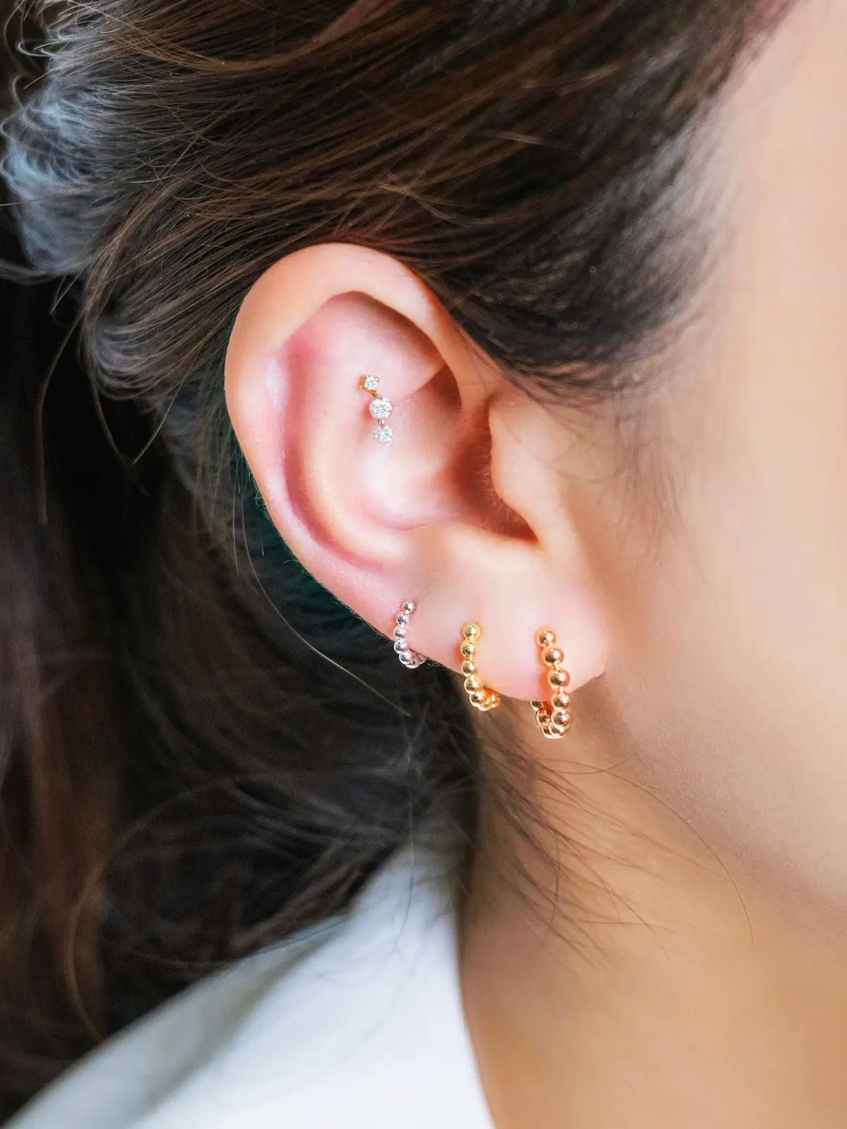 Close-up of woman’s ear with multiple hoop earrings and a helix stud