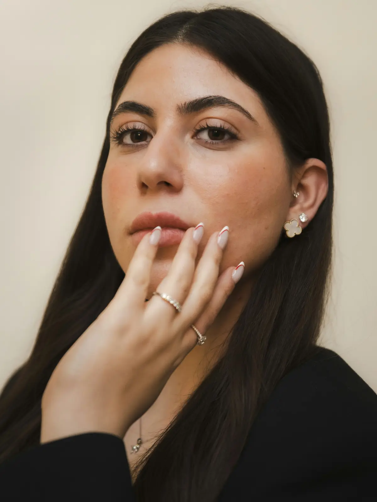 Studio shot of a woman with lobe and tragus piercings holding a manicured hand to her face