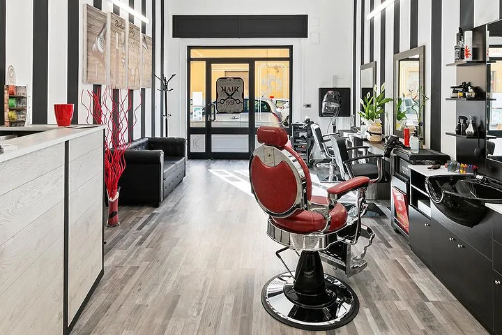 Red vintage barber chair at Hair 99 in Alghero with signature black-and-white striped walls.