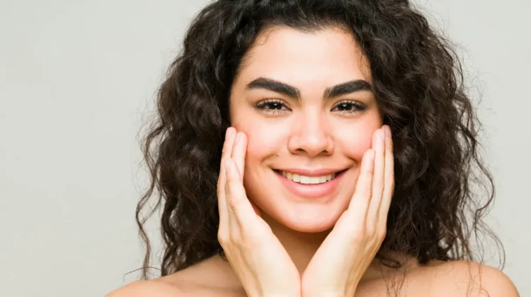 A young woman with clear skin and dark wavy hair smiles at the camera