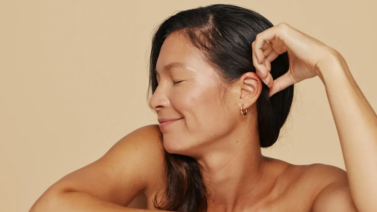 Woman pictured from shoulders up, smiling with her eyes closed and looking relaxed and refreshed as she looks to the side