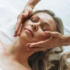 Woman relaxing during a gentle lymphatic drainage facial massage with therapist's hands lightly gliding across her face