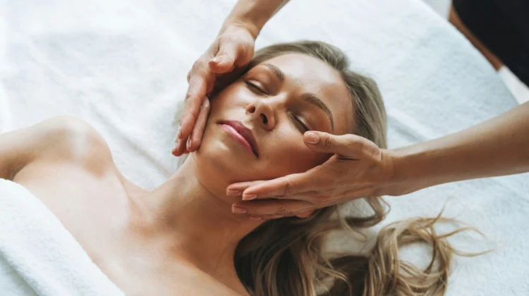 Woman relaxing during a gentle lymphatic drainage facial massage with therapist's hands lightly gliding across her face