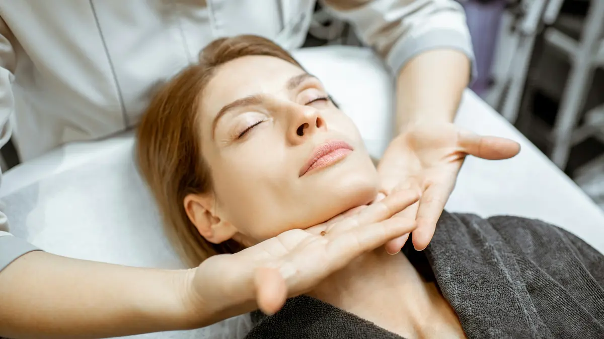Woman relaxing during a gentle lymphatic drainage facial massage with therapist's hands lightly gliding under her jaw