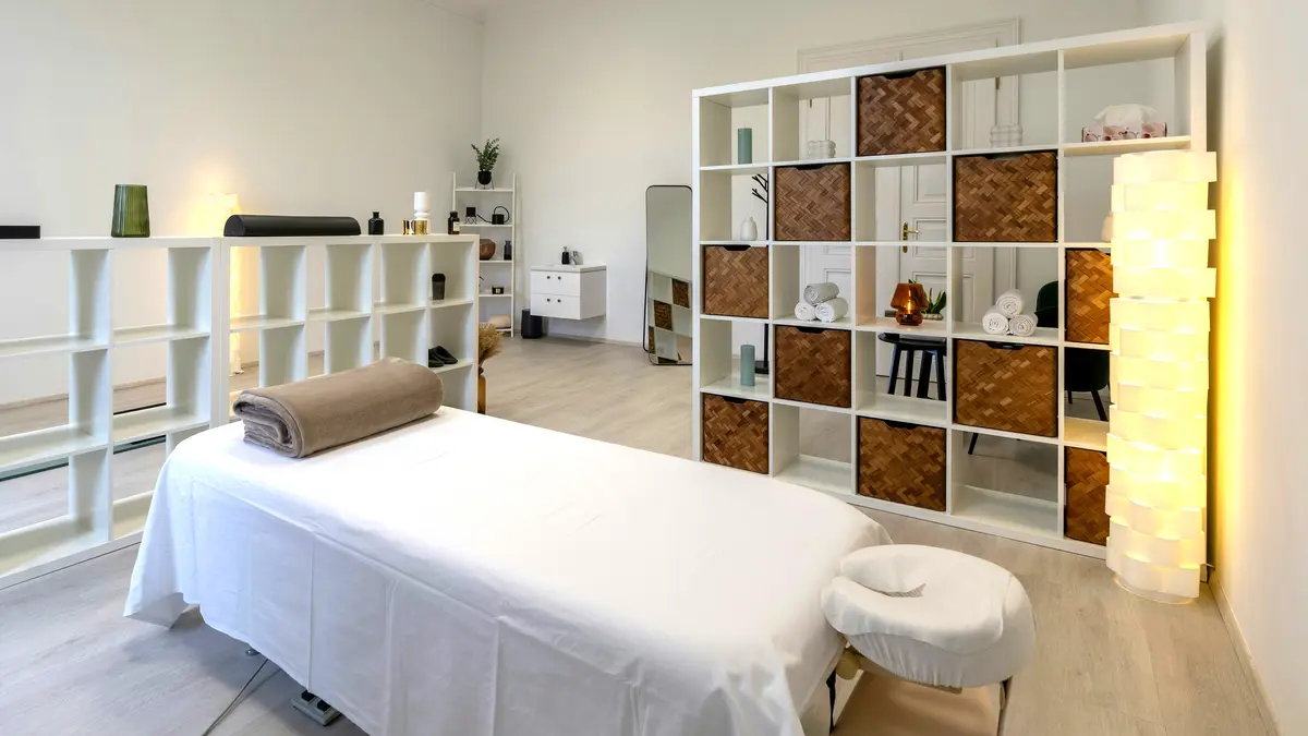 A clean and tidy treatment room in a salon with a treatment bed laid with sheets and a rolled blanket ready for a massage treatment